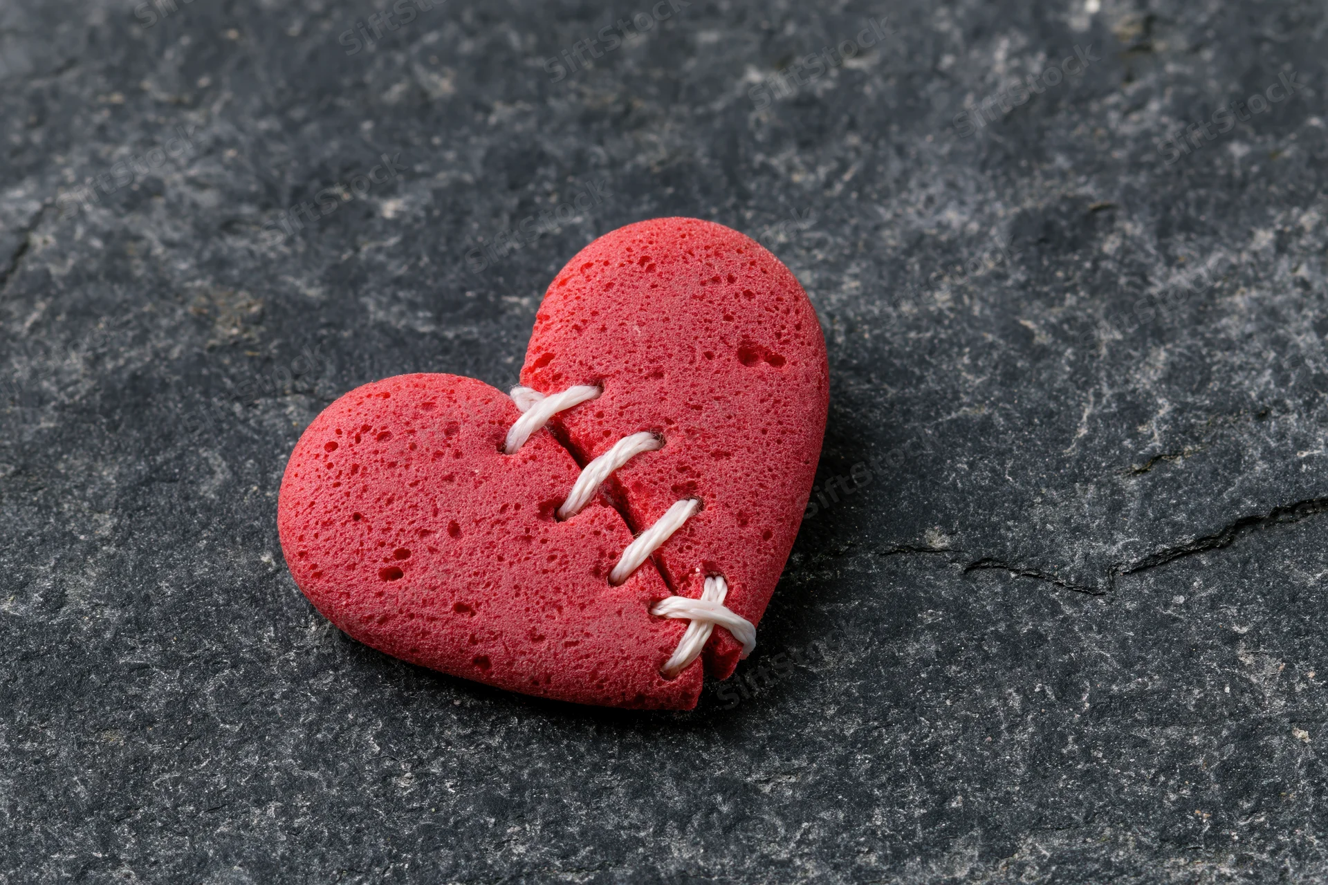 Red foam heart stitched back together on dark stone surface