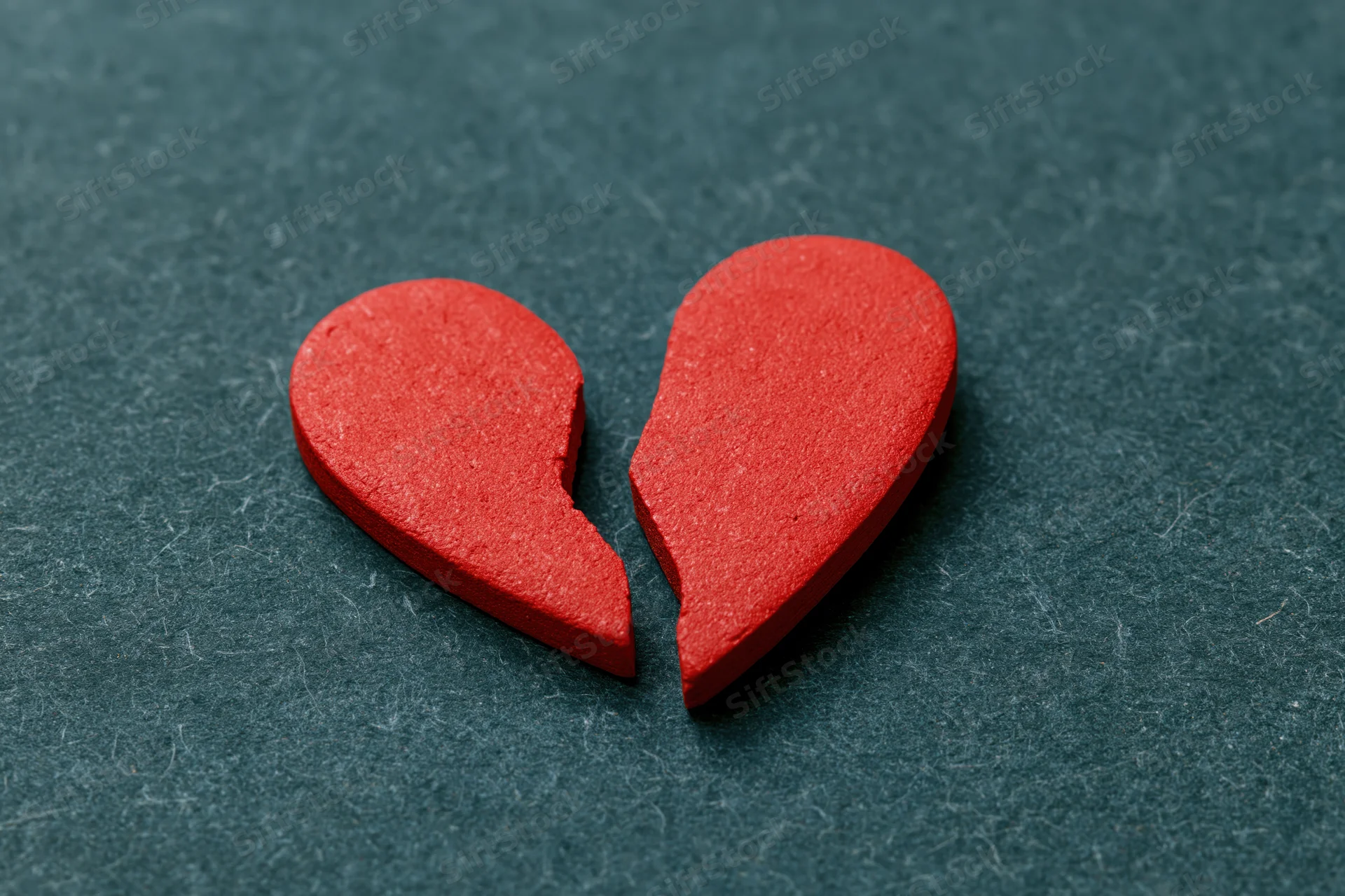 Broken red heart symbol split in two on dark textured surface