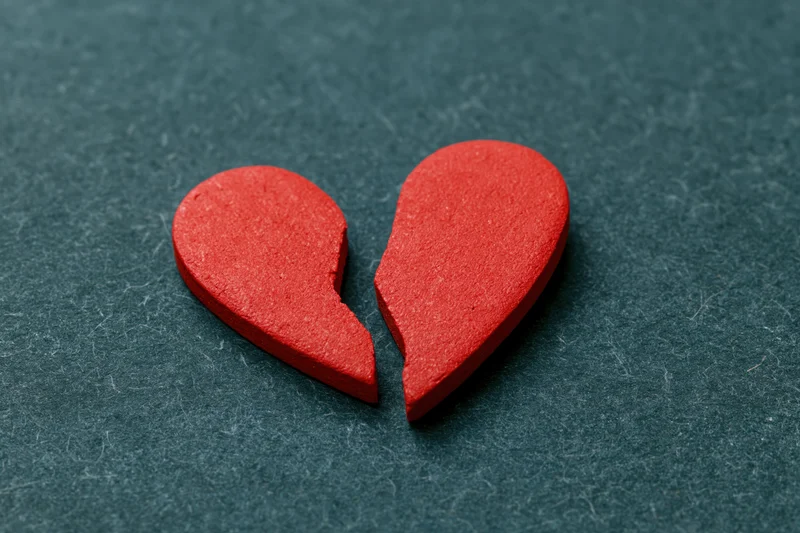 Broken red heart symbol split in two on dark textured surface