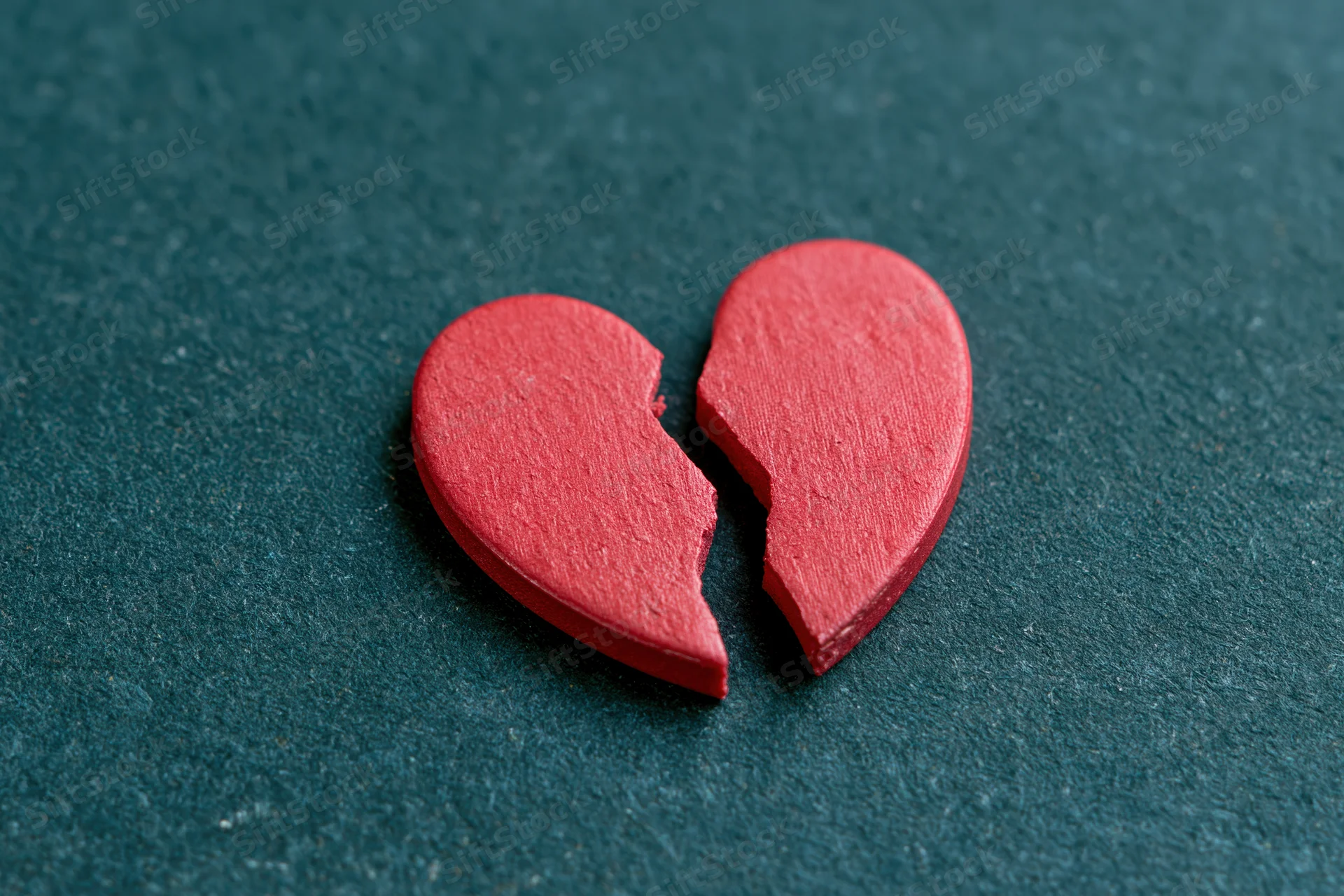 Broken red wooden heart lying on dark textured surface