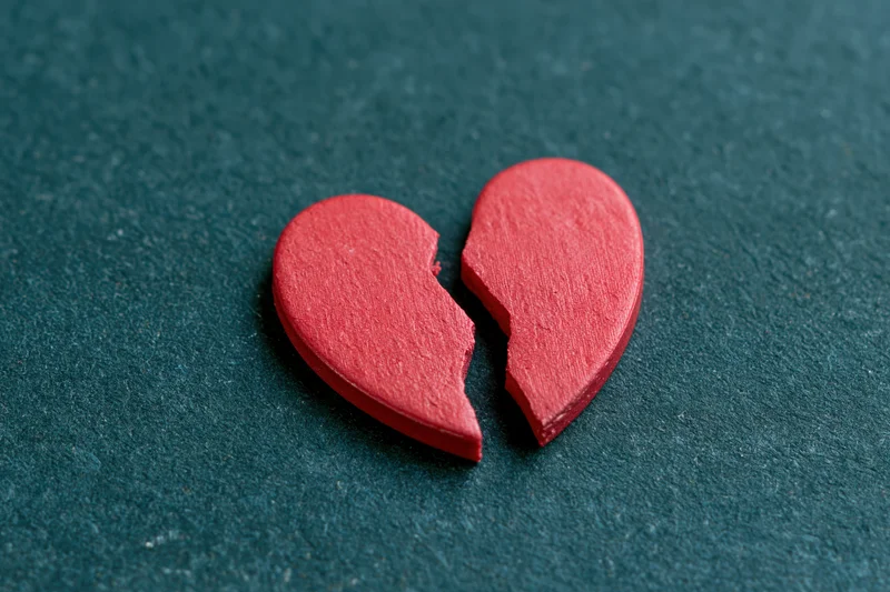 Broken red wooden heart lying on dark textured surface