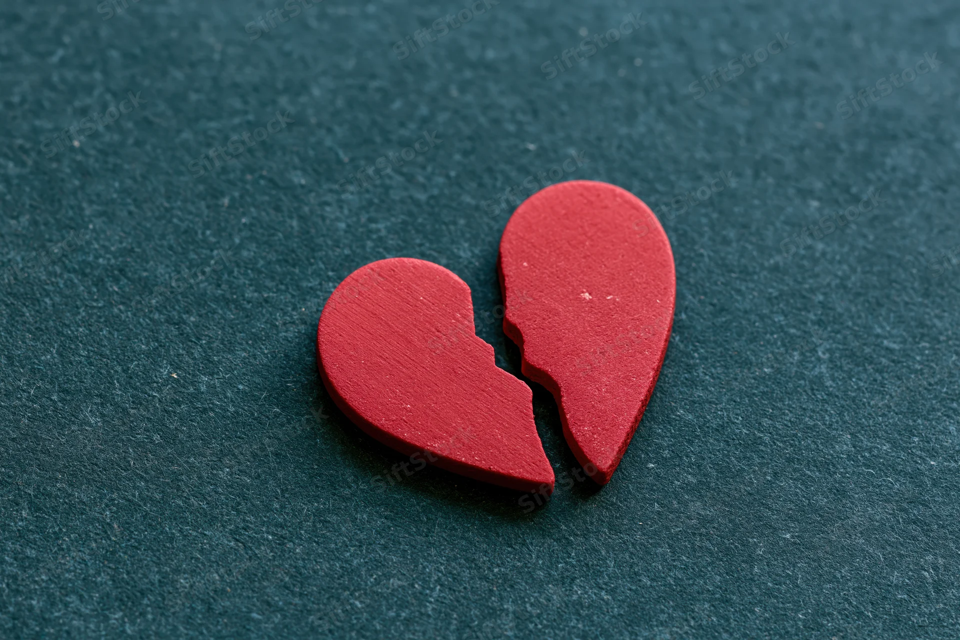 Broken red heart symbol split in two on dark textured surface