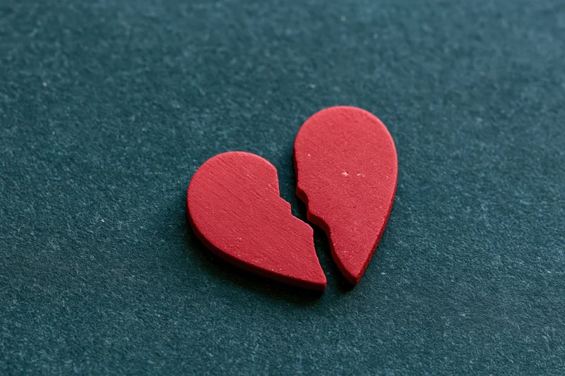 Broken red heart symbol split in two on dark textured surface