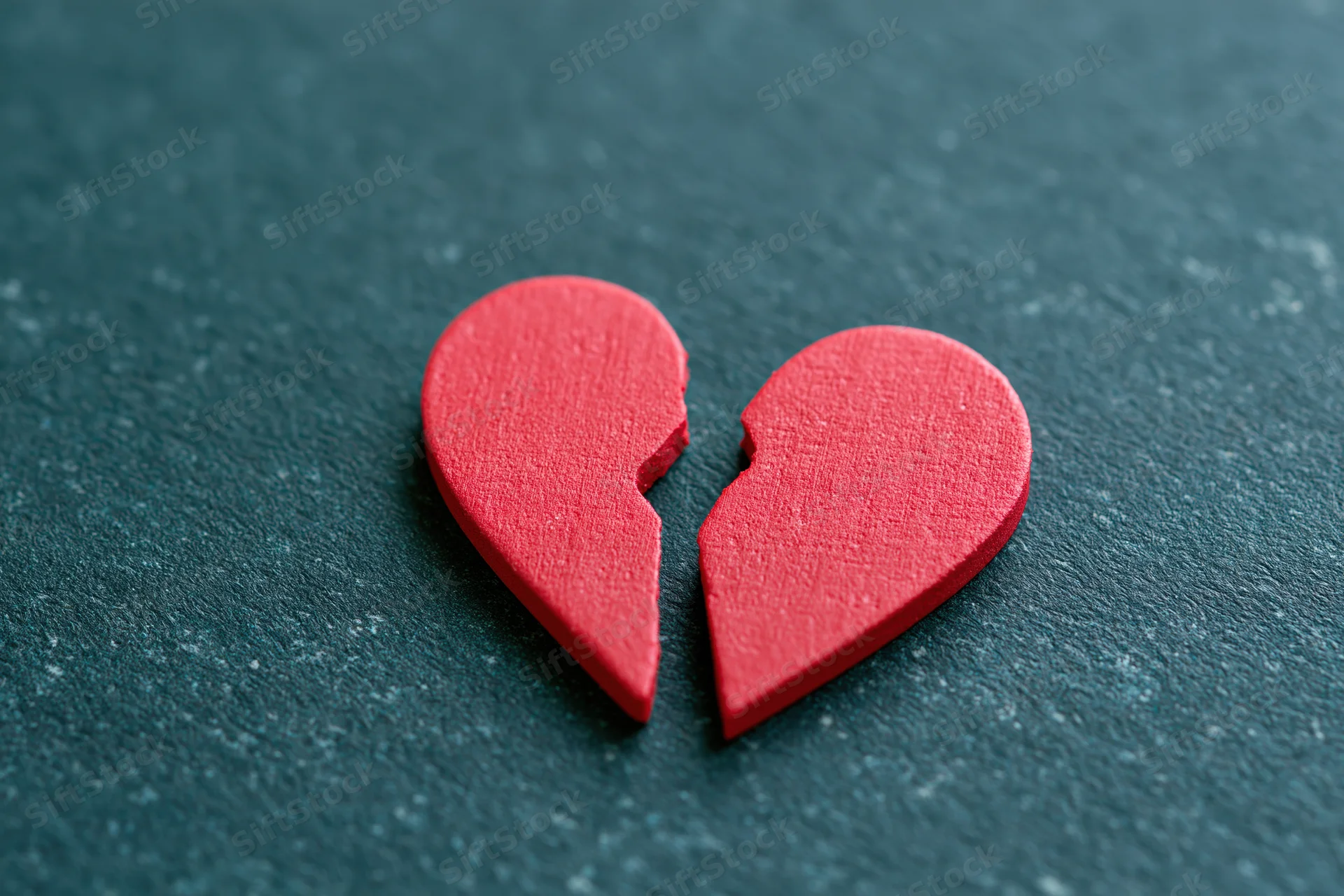 Broken red heart symbol on dark textured surface