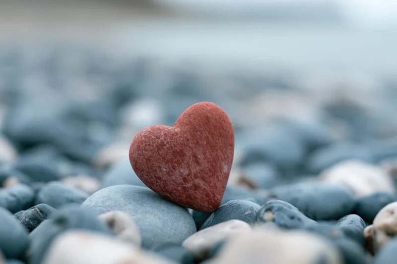Red heart-shaped stone resting upright among smooth pebbles on a beach