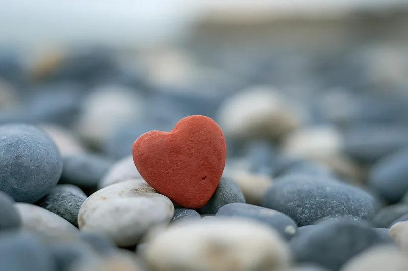 Red heart-shaped stone resting among smooth pebbles on a beach
