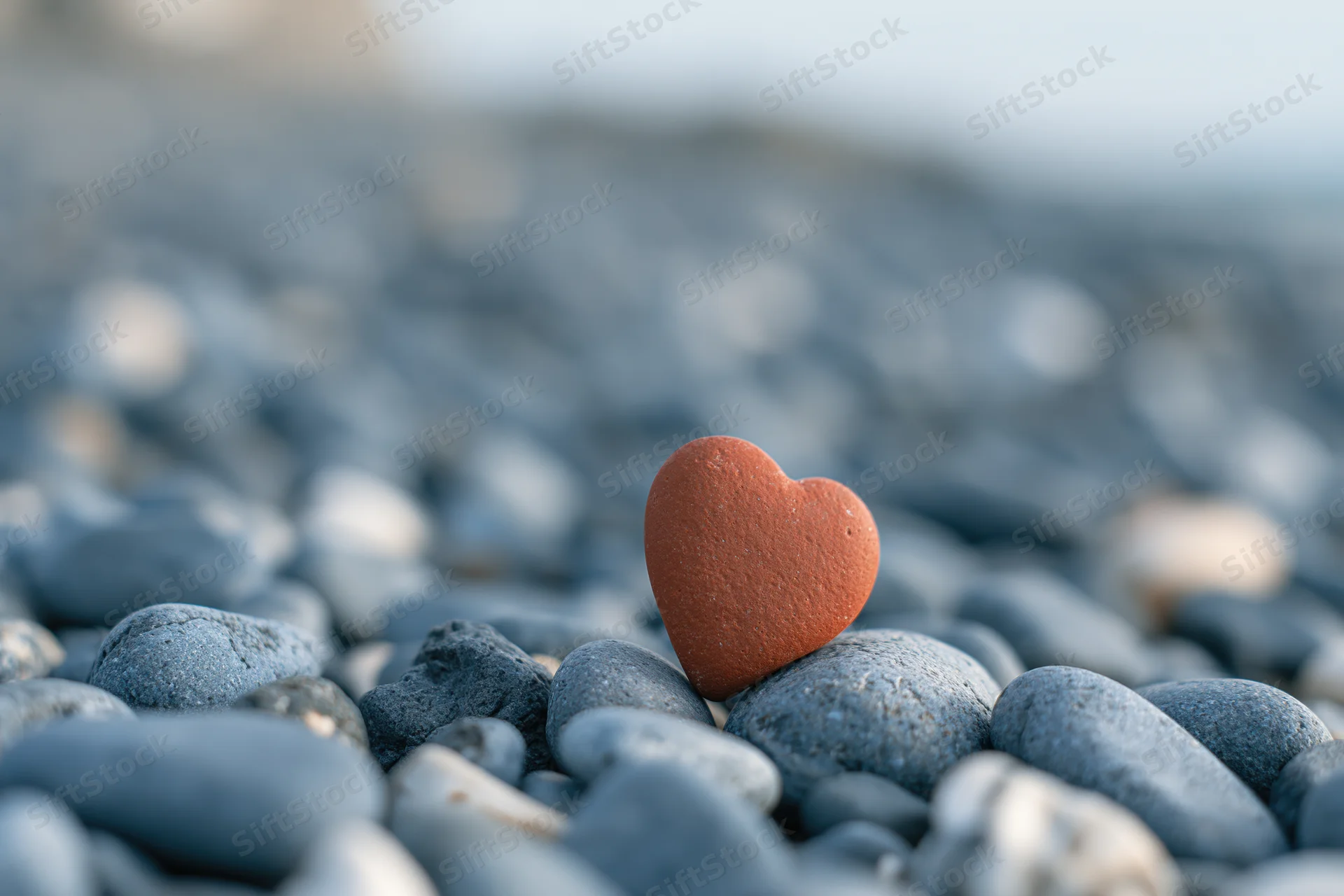 Red heart-shaped stone resting upright among smooth pebbles on a beach
