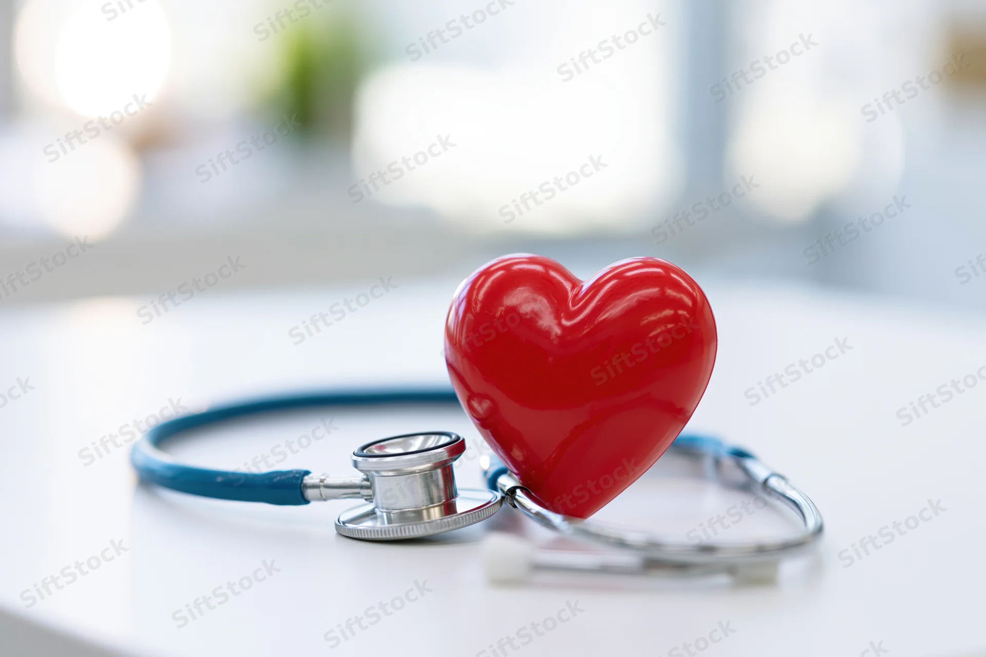 Red heart prop leaning against blue stethoscope on white surface in clinic setting