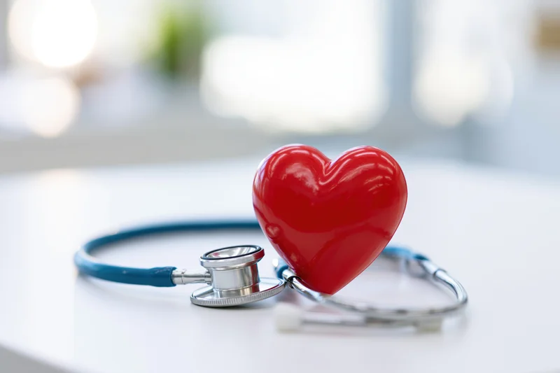 Red heart prop leaning against blue stethoscope on white surface in clinic setting