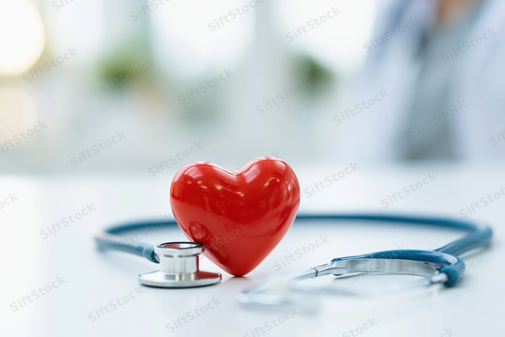 Red heart prop leaning against blue stethoscope on white surface in clinic setting
