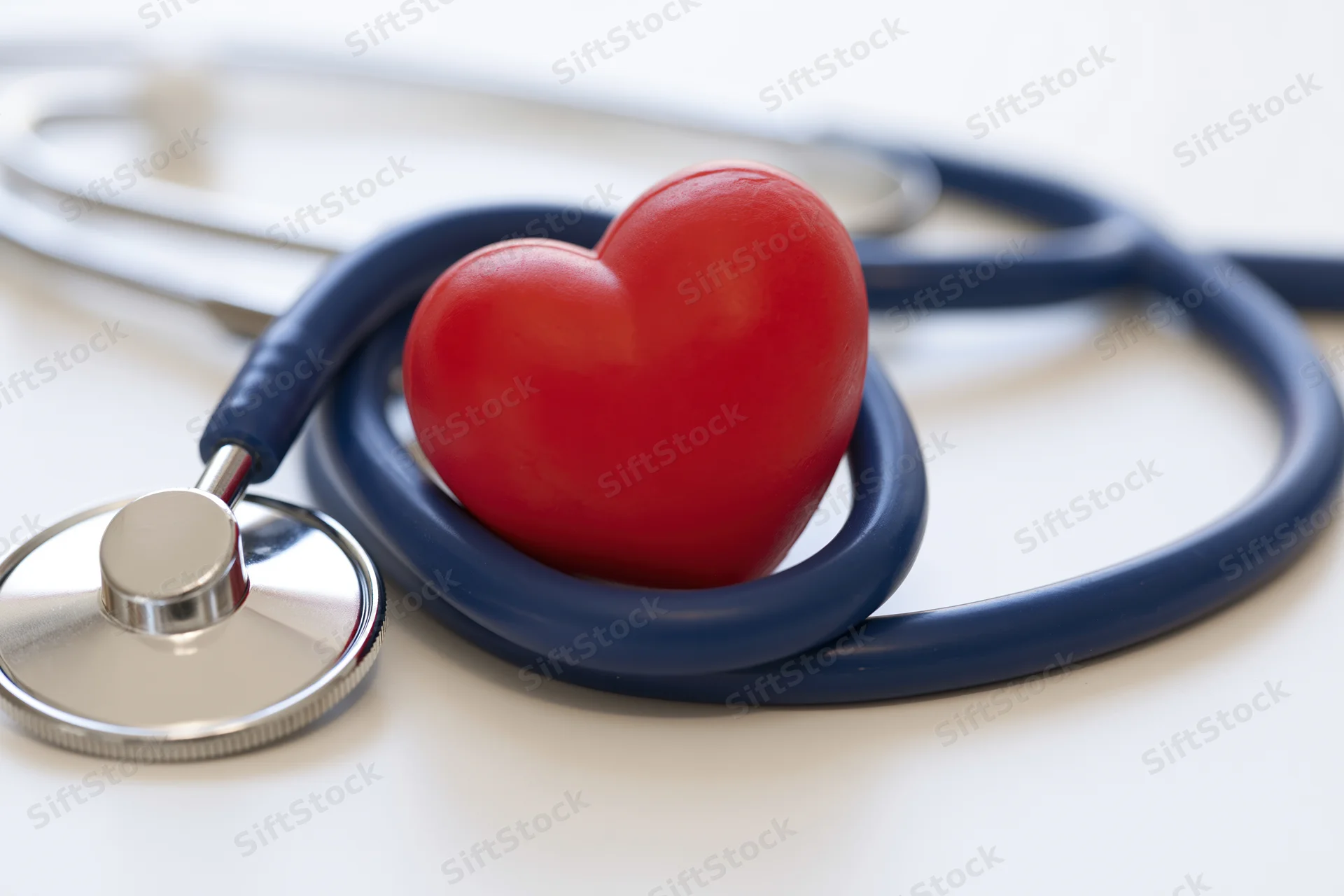 Red heart-shaped stress toy resting inside looped stethoscope tubing on white surface