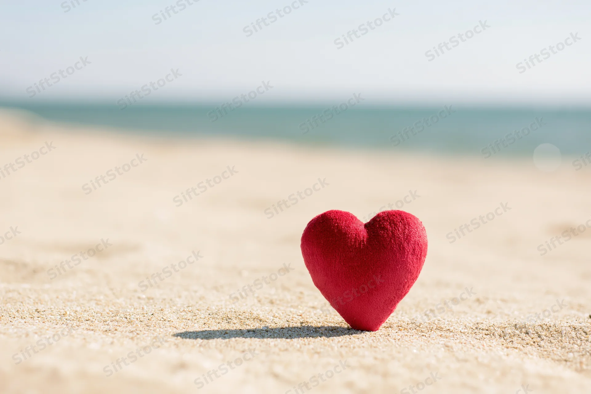 Red velvet heart standing upright on sandy beach near ocean