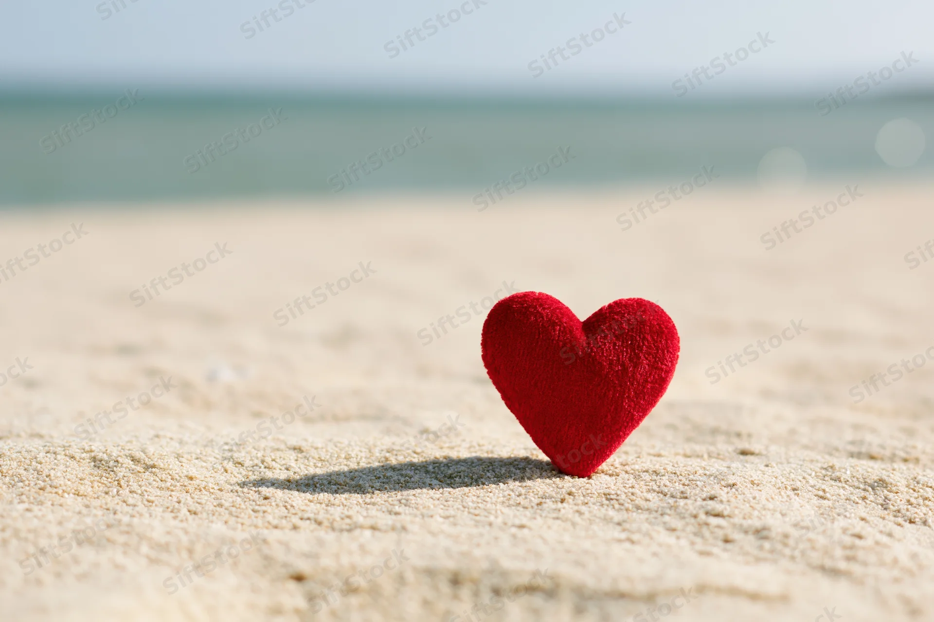 Red velvet heart standing upright on sandy beach near ocean