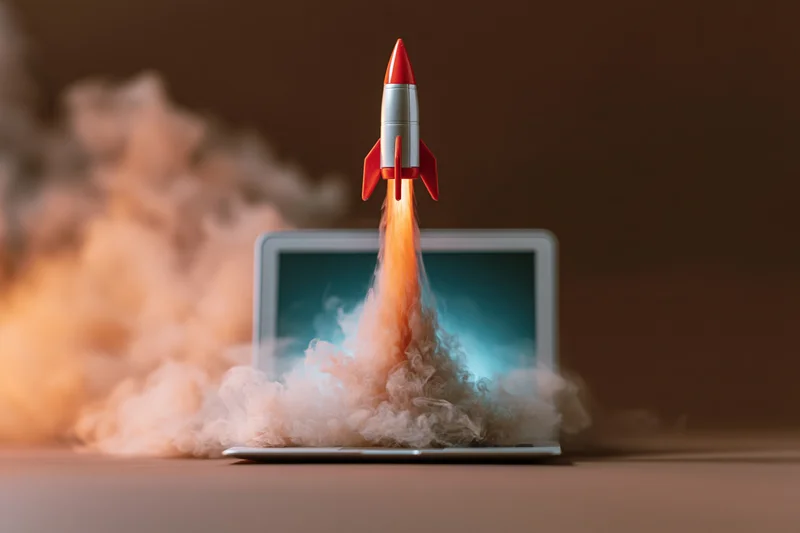 Small red and white rocket launching from open laptop screen with smoke and flame
