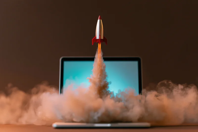 Toy rocket launching from laptop screen surrounded by smoke
