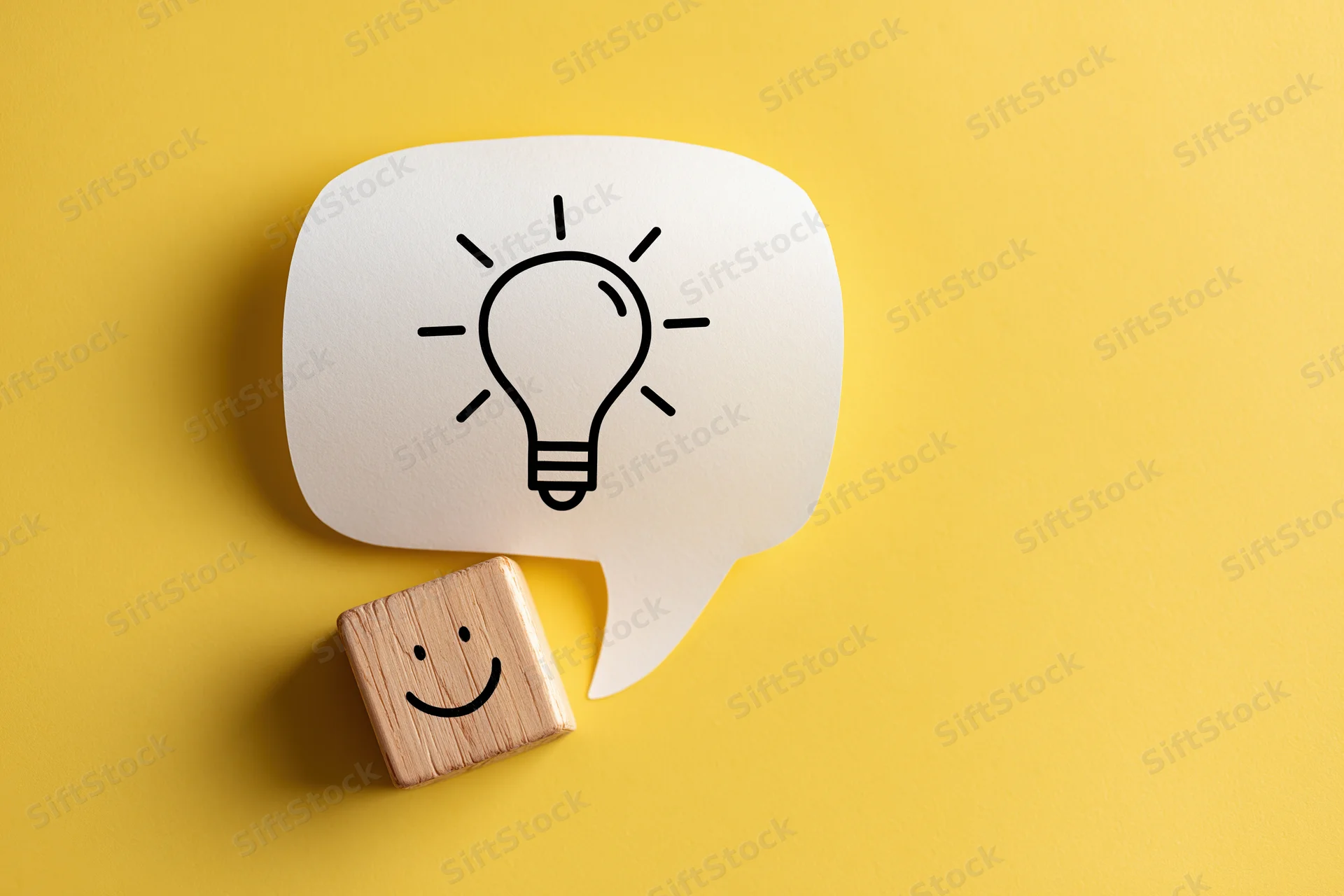 Wooden block with smiley face beside a speech bubble containing a lightbulb on yellow background