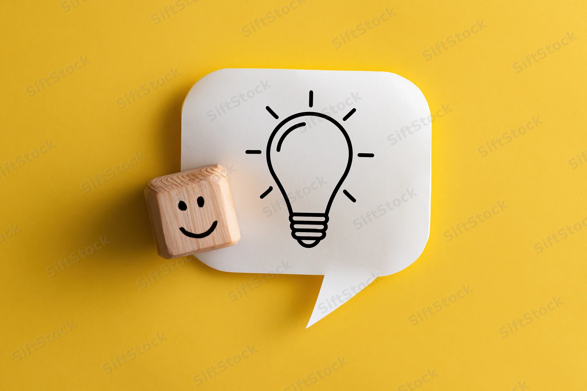 Wooden cube with smiley face next to speech bubble containing lightbulb on yellow background