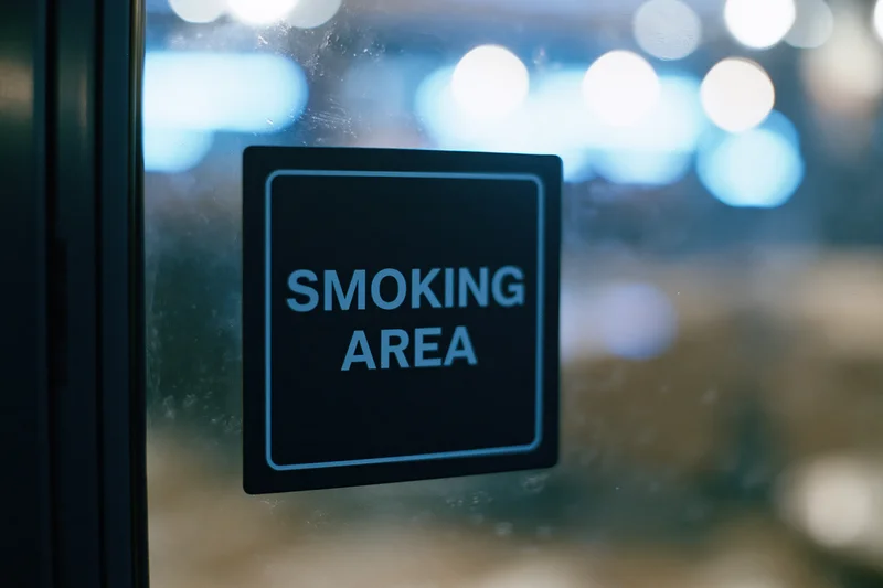 Black square smoking area sign with blue lettering on glass door at night