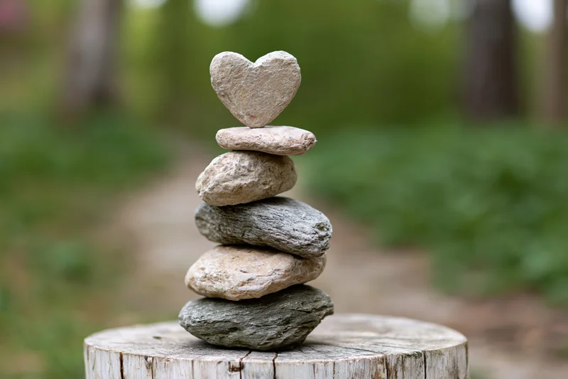 Heart-shaped stone balanced atop a stack of river stones on a tree stump in a forest setting