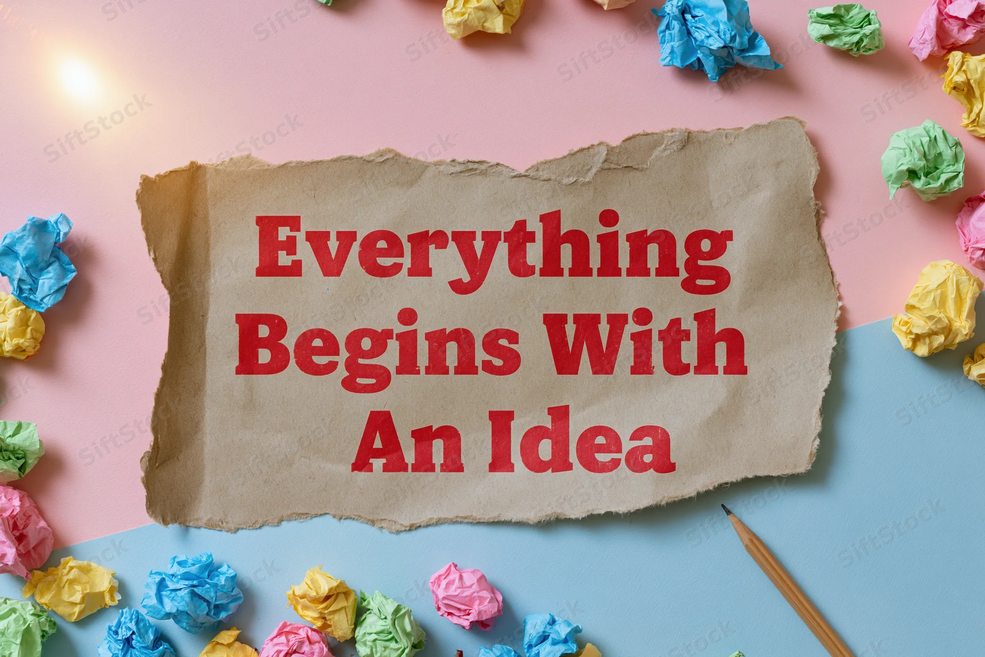 Torn kraft paper with red text reading everything begins with an idea surrounded by crumpled colorful papers and a pencil on pink and blue background