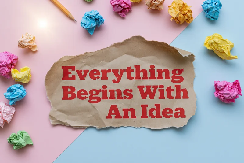 Torn kraft paper with red text reading everything begins with an idea surrounded by crumpled colorful papers and a pencil on pink and blue background