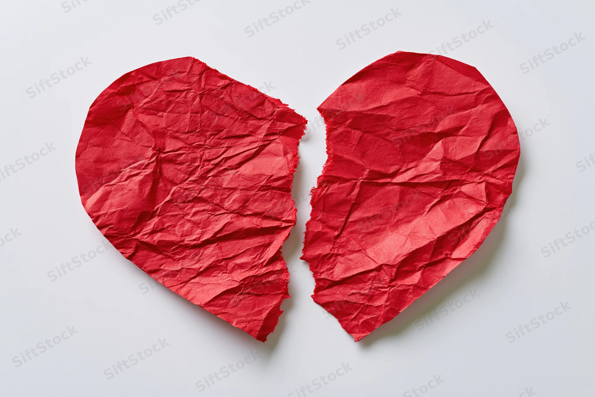 Torn red paper heart split into two halves on white surface