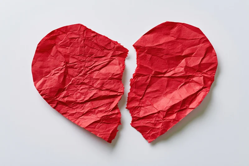 Torn red paper heart split into two halves on white surface