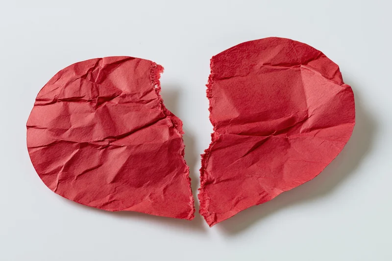 Torn red paper heart split into two halves on white surface