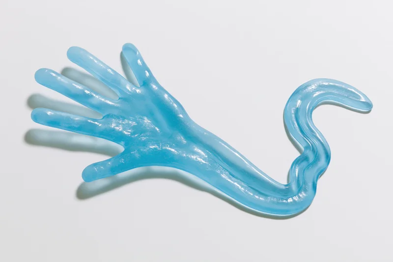 Translucent blue rubber hand toy with elongated tail lying flat on white surface