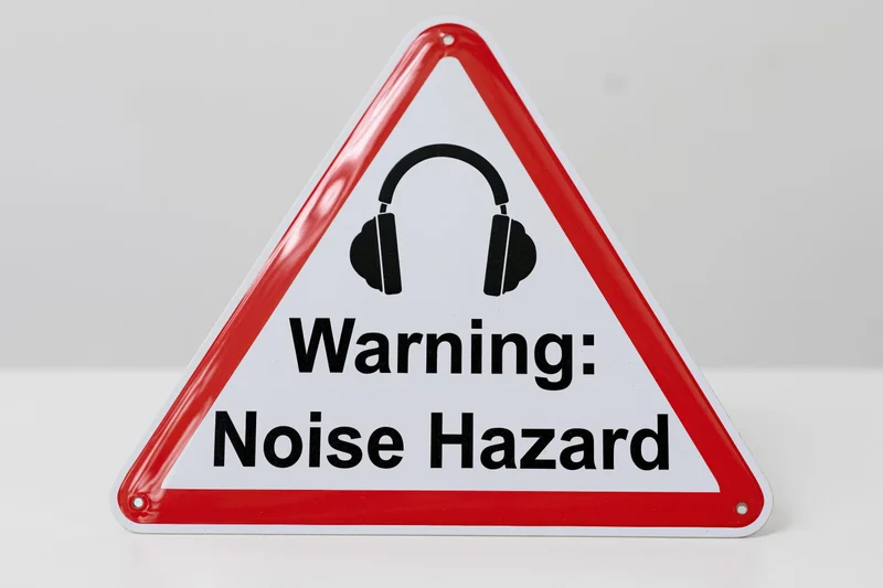 Triangular warning sign with red border and headphones symbol indicating noise hazard