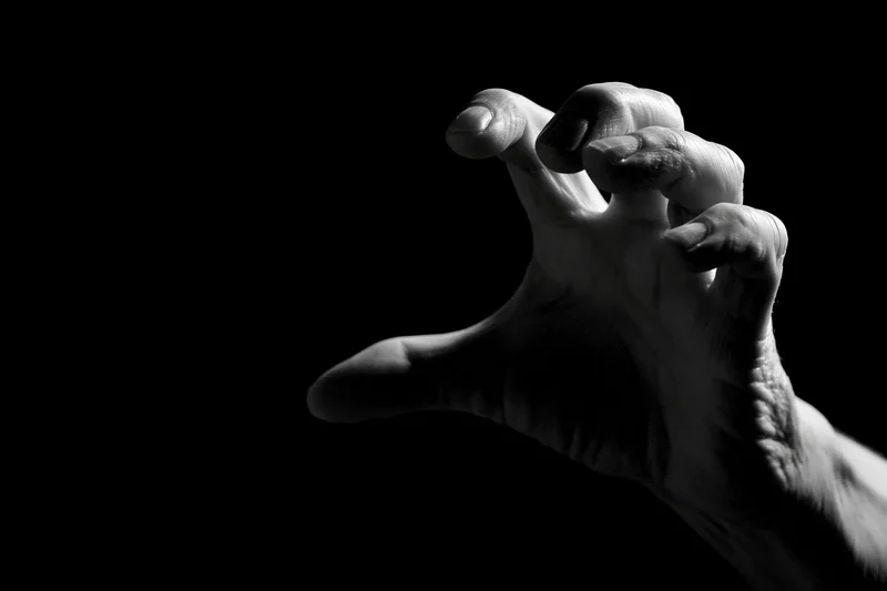 Weathered hand reaching forward with fingers curled in a grasping gesture against black background