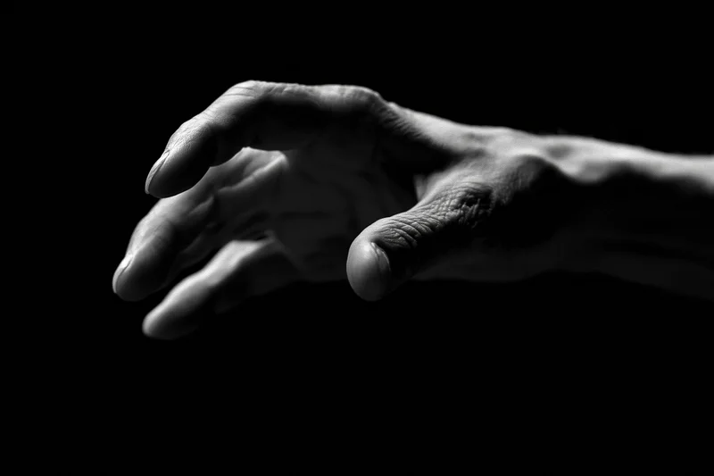 Weathered hand reaching forward against black background
