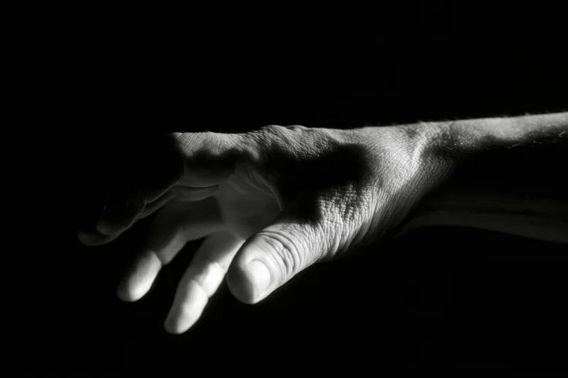 Weathered hand reaching forward against black background