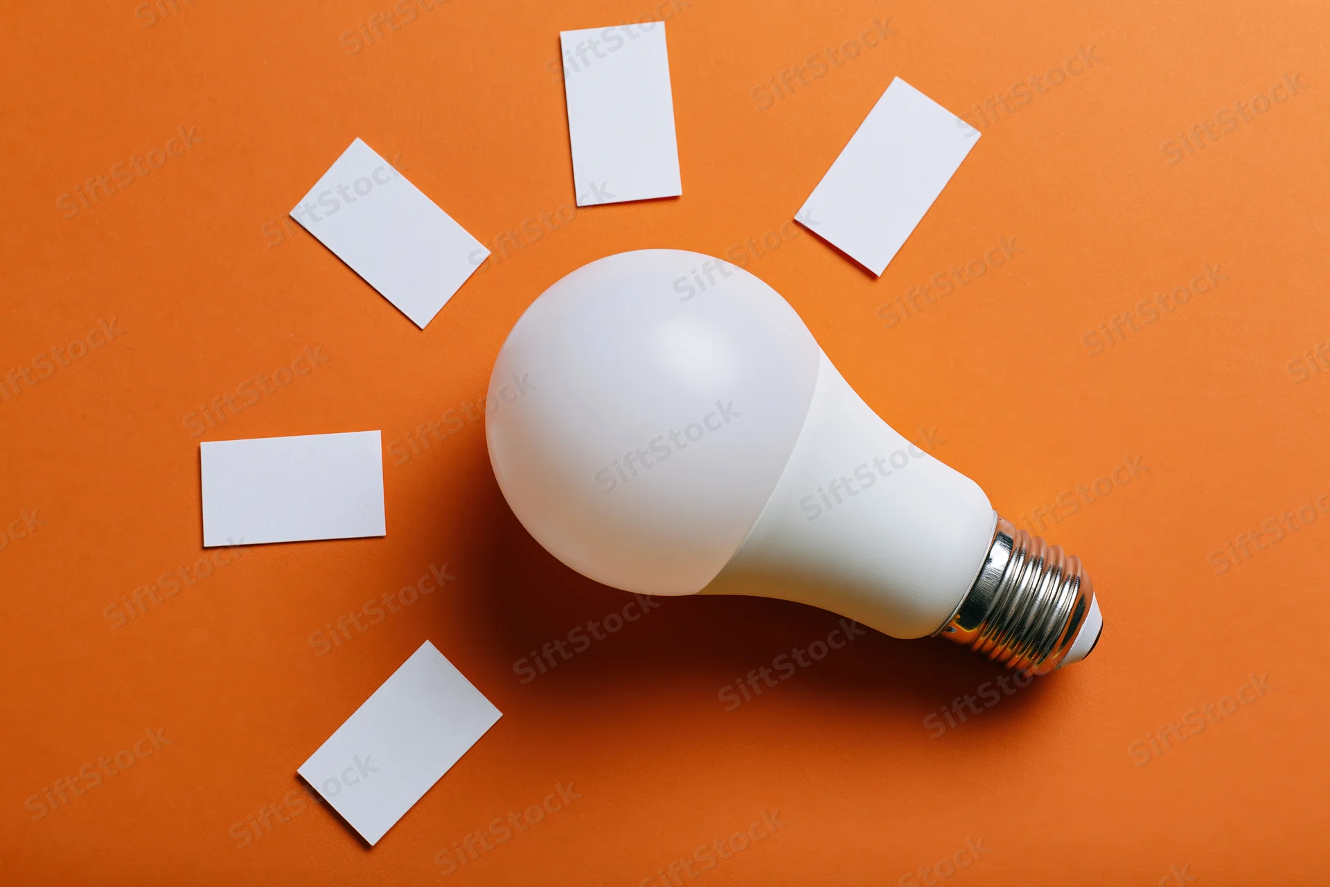 White led lightbulb on orange paper with blank cards arranged around it