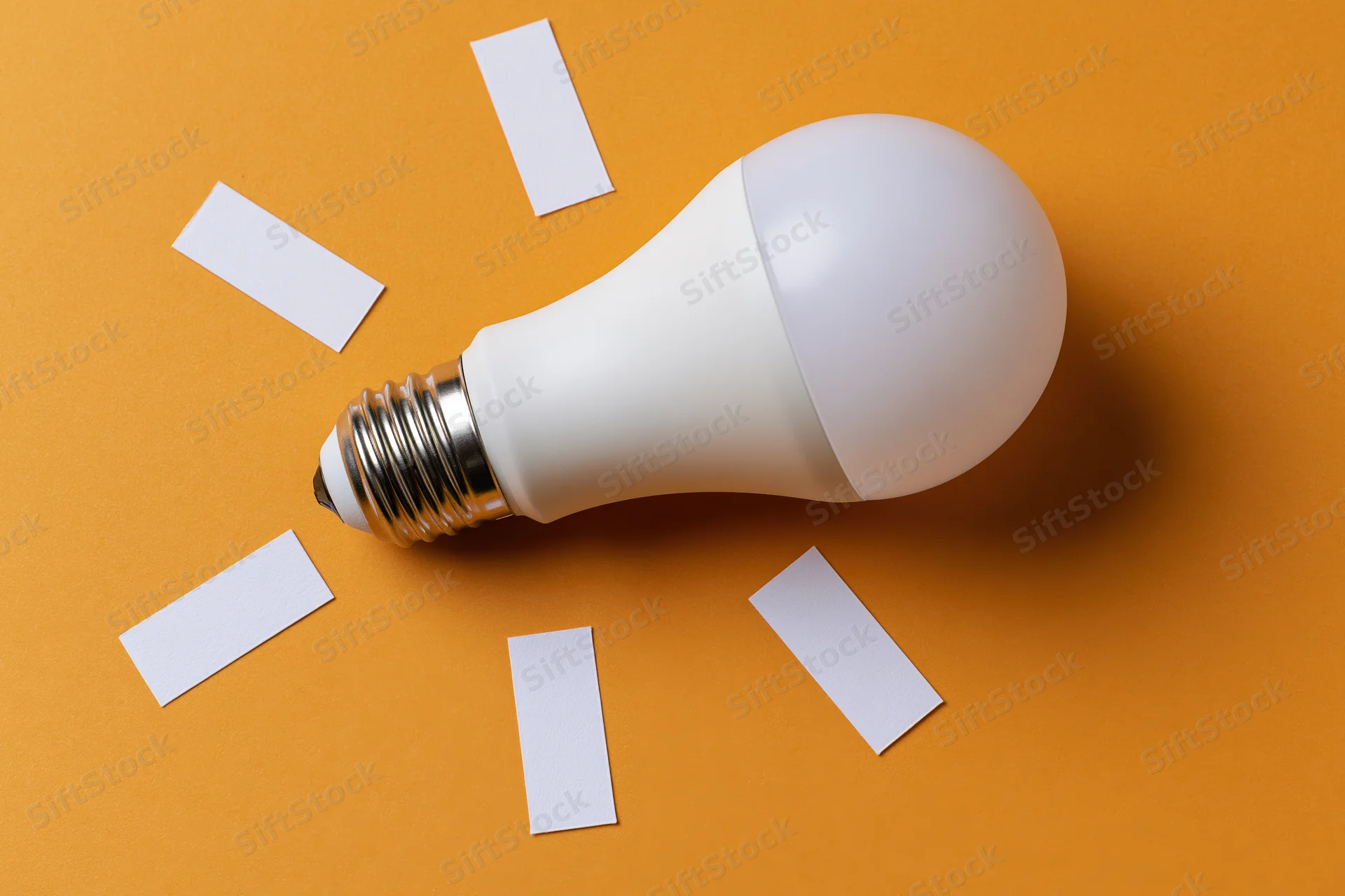 White led lightbulb lying flat on orange paper with scattered white rectangles around it