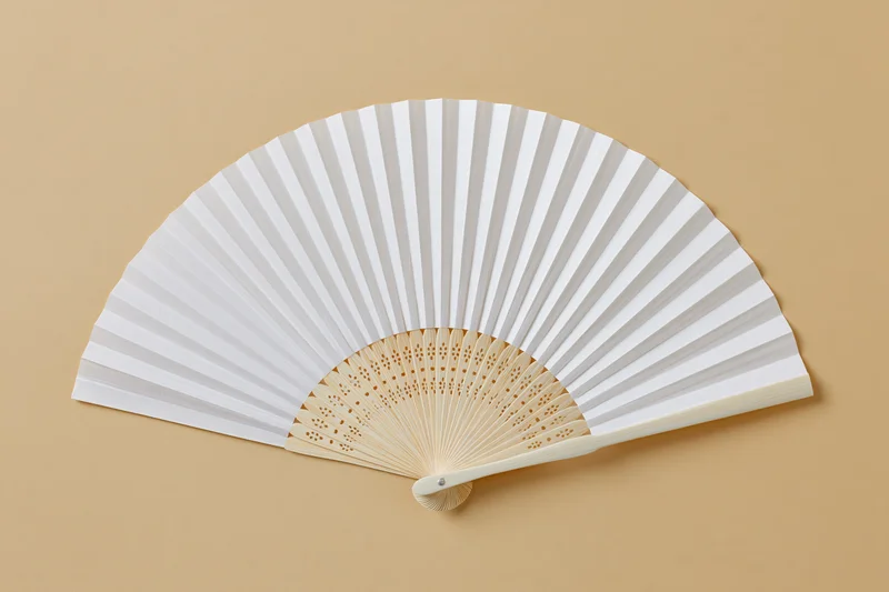 Open white paper hand fan with bamboo ribs laid flat on beige background