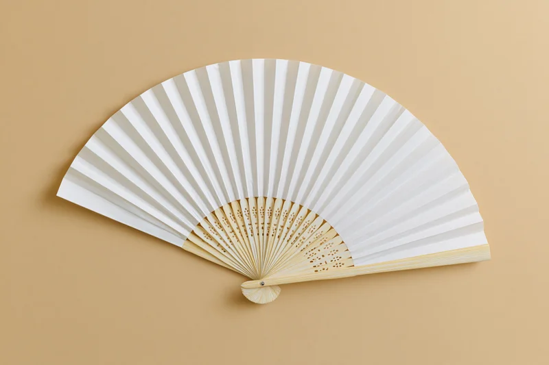 Open white paper fan with bamboo frame lying flat on beige surface