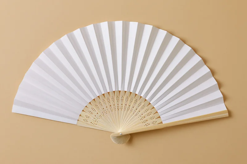 White paper hand fan fully opened and laid flat on beige background
