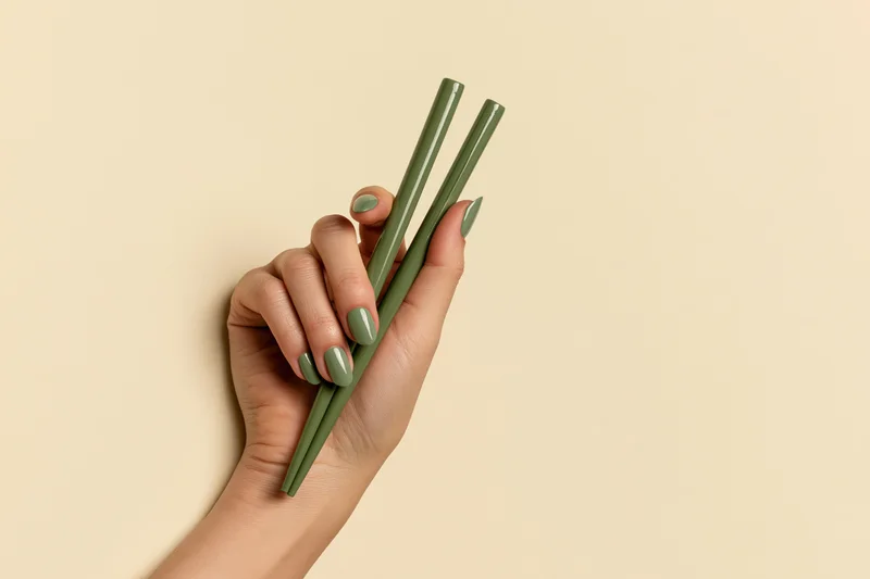 Woman's hand holding green chopsticks against beige background
