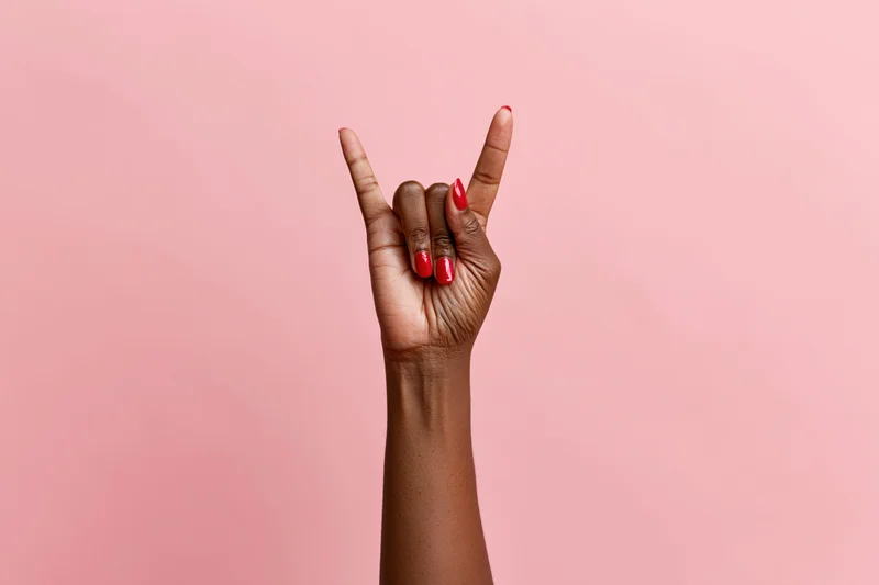 Woman's hand making rock sign gesture against pink studio backdrop