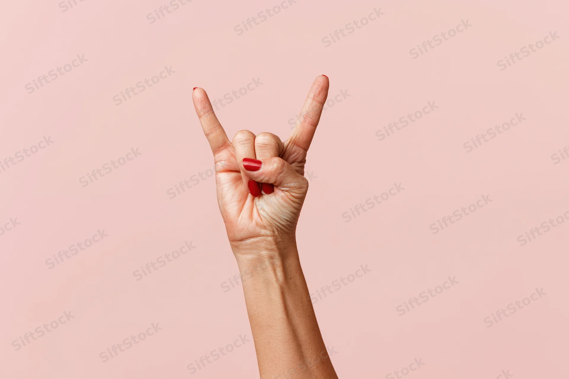 Woman's hand making rock gesture against pink studio backdrop