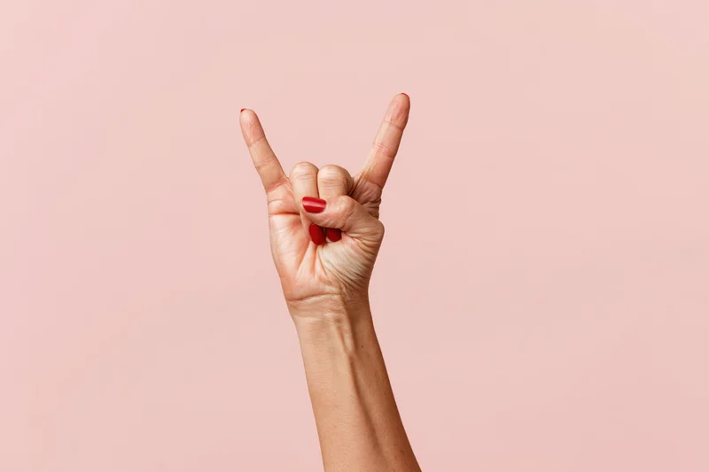 Woman's hand making rock gesture against pink studio backdrop