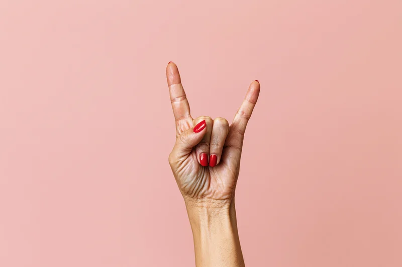 Woman's hand making rock sign gesture against pink studio backdrop