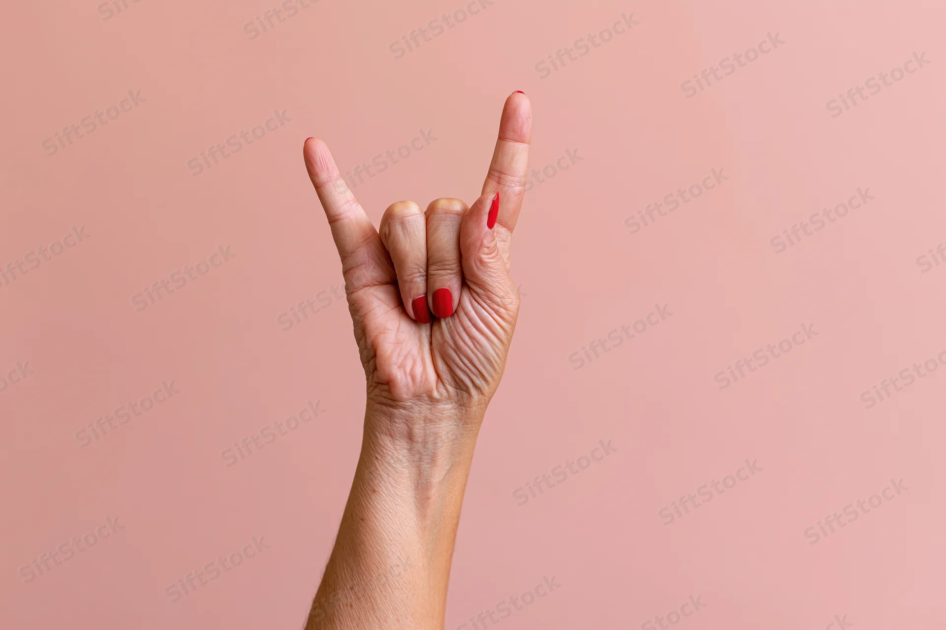 Woman's hand making rock sign gesture against pink studio backdrop