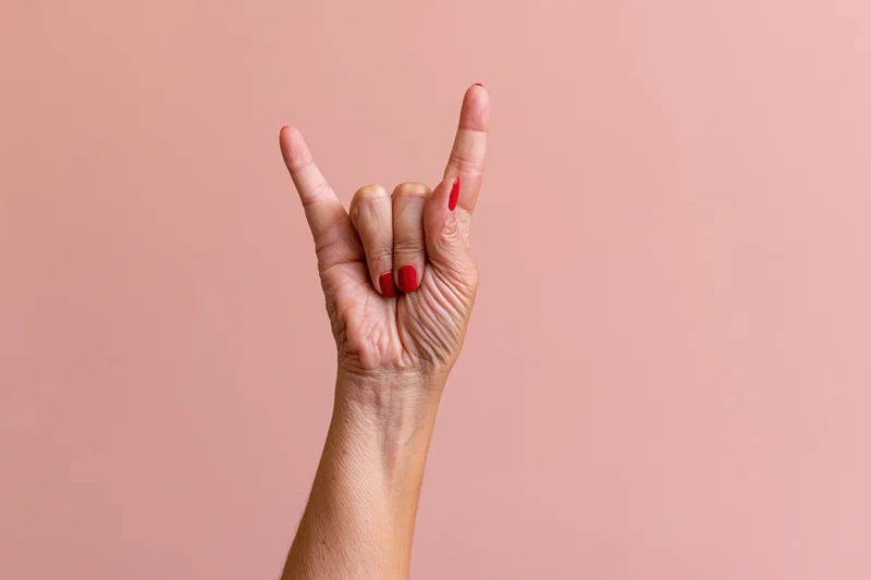 Woman's hand making rock sign gesture against pink studio backdrop