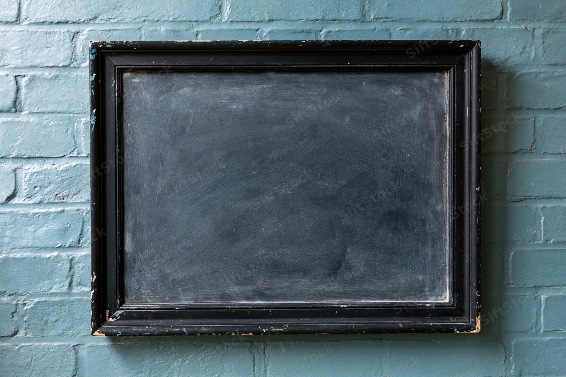 Worn black chalkboard with wooden frame mounted on teal brick wall