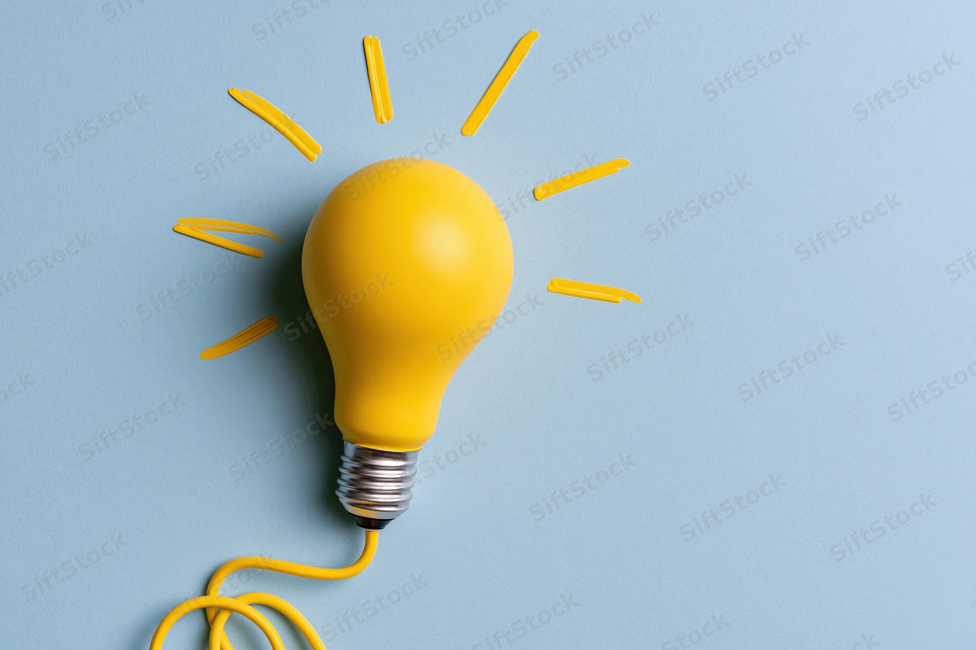 Yellow painted lightbulb with radiating lines on pale blue paper background