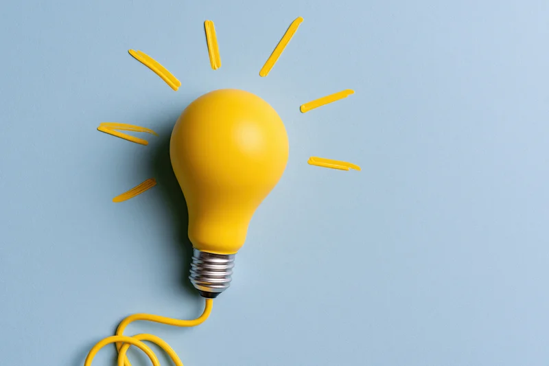 Yellow painted lightbulb with radiating lines on pale blue paper background