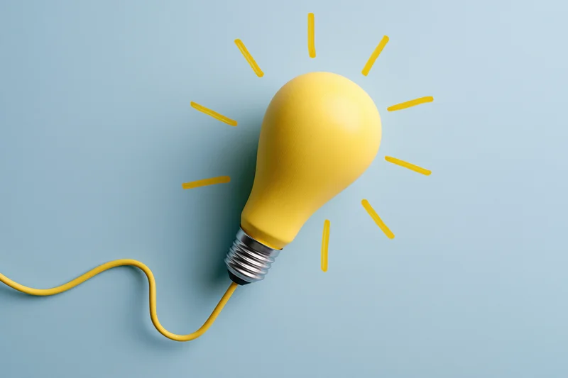 Yellow painted lightbulb with radiating lines on pale blue paper surface