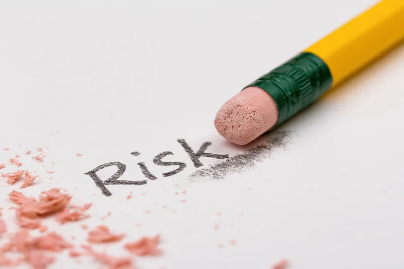 Yellow pencil eraser rubbing out the word risk on white paper